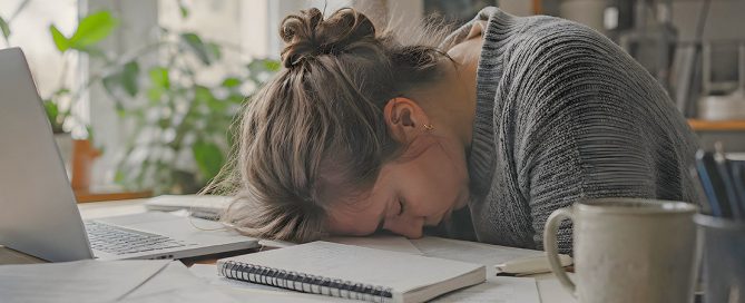 Estudiante agotado frente a libros y ordenador con expresión de agotamiento mental representando el burnout académico