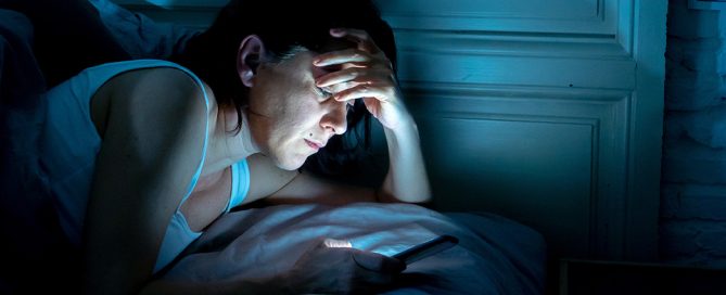 Persona tumbada mirando el móvil con expresión ansiosa mientras su pareja está fuera, representando los celos y la ansiedad de separación en pareja.