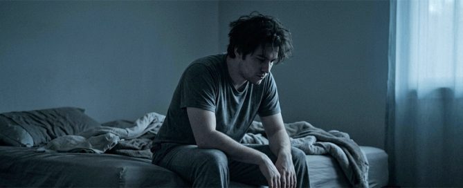 Persona sentada en el borde de la cama en la oscuridad con la cabeza inclinada representando la rumiación nocturna y los pensamientos que no paran de noche