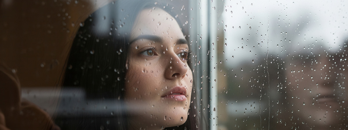 Persona apagada junto a una ventana en una tarde gris de otoño, representando la depresión estacional